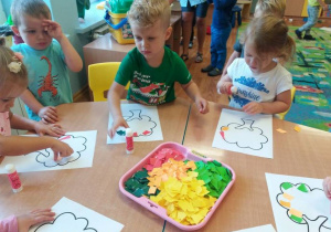 Dzieci przy stoliku wyklejają kontury drzewa kolorowymi kawałkami papieru
